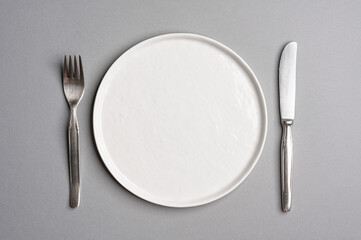White flat empty plate with cutlery on a light gray background. Top view.