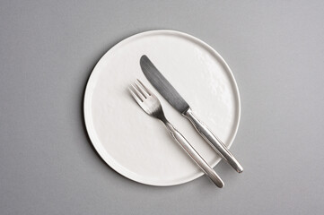 White flat empty plate with cutlery on a light gray background. Top view.