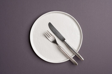 White flat empty plate with cutlery on a dark gray background. Top view.