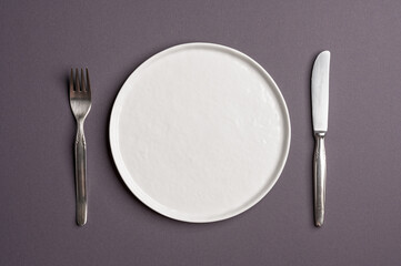 White flat empty plate with cutlery on a dark gray background. Top view.
