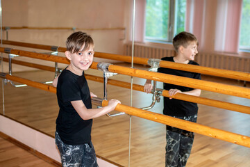 a boy in sports black clothes stands at the choreographic barre in the dance hall