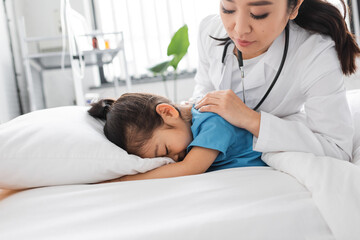 Obraz premium asian doctor calming depressed child obscuring face with pillow on hospital bed.
