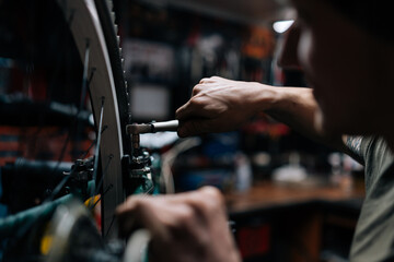 Close-up cropped shot of unrecognizable craftsman repairing bike using special tool working in bicycle repair shop with dark interior. Concept of professional repair and maintenance of bicycle.