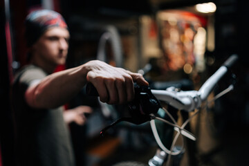 Fototapeta na wymiar Close-up hands of unrecognizable mechanic insisting speed switches on mountain bike handlebar working in bicycle repair shop with dark interior. Concept of professional repair and maintenance of bike.