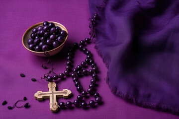 Against a violet fabric background, a rosary serves as a symbol of penance and reflection on the religious concept of Ash Wednesday.