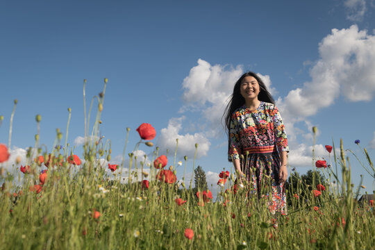 happy asian girl in floral dress smiling in poppy field in summer