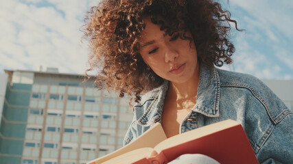 Close-up of a young woman reading a book. Student studying while sitting outside the university...
