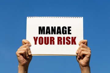 Manage your risk text on notebook paper held by 2 hands with isolated blue sky background. This message can be used as business concept about managing your risk.