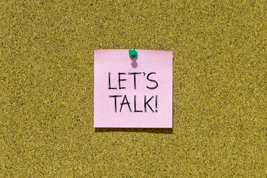 Let's talk text on pink post-it paper pinned on bulletin cork board. This message can be used in business concept about talking together.