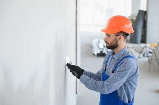 man drywall worker or plasterer sanding and smoothing a plasterboard walls with stucco using a sandpaper holder. Wearing white hardhat and safety glasses. Panoramic image with copy space