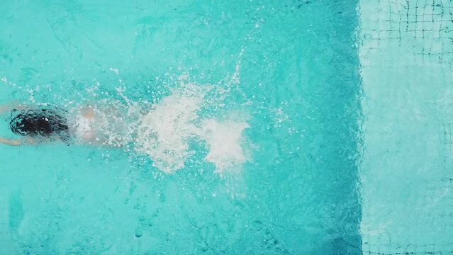 Aerial view of Active woman, girl jumping in swimming pool, drone view from above, young woman swims in blue water, Bali villa, tropical vacation, holiday on island hotel resort