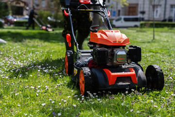 Communal services gardener worker man using lawn mower for grass cutting in city park.