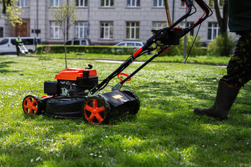 Communal services gardener worker man using lawn mower for grass cutting in city park.