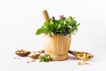 Wooden morfar with mix of medical herbs and spoons with tablets, pills and capsules on white background. Alternative herbal medicine concept.