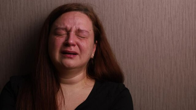 Distressed woman bitterly cry near room wall. Tears roll down cheeks, tearful eyes and swollen face. Splash out emotions, sob violently. Emotional breakdown, sufferings. Depression and hysterics.