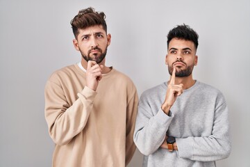 Young homosexual couple standing over white background thinking concentrated about doubt with...