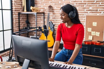Fototapeta na wymiar Young african american woman musician playing piano keyboard at music studio