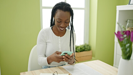 African american woman using smartphone sitting on table at home