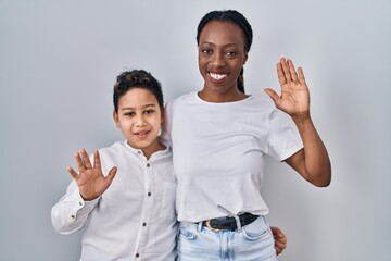 Young mother and son standing together over white background waiving saying hello happy and...