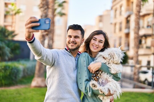 Man and woman holding dog making selfie by the smartphone at park
