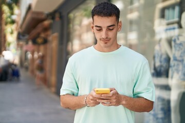 Young hispanic man using smartphone with serious expression at street