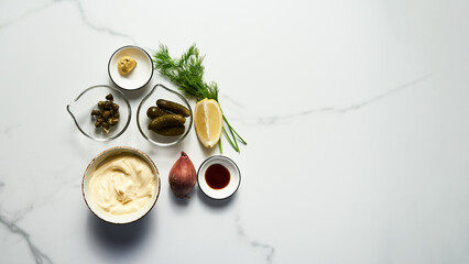 Obraz na płótnie Canvas Classic Tartar Sauce ingredients on white marble background. Mayonnaise with dill and capers plus lemon, shallot onion. Worcester sauce and Dijon Mustard. Top view food photo. Flatlay