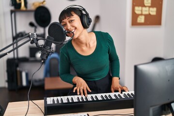 Young beautiful hispanic woman musician singing song playing piano at music studio