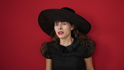 Young caucasian woman looking afraid wearing witch costume over isolated red background