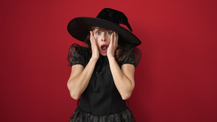 Young caucasian woman looking afraid with hands on face wearing witch costume over isolated red background