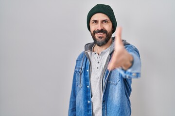 Young hispanic man with tattoos wearing wool cap smiling friendly offering handshake as greeting and welcoming. successful business.