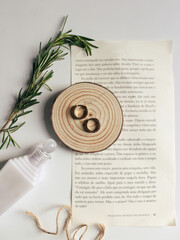 Composition with female accessories. Moisturizing lotion, a pair of small earrings and wood pieces on a page of a book on the white background. Jewelry minimalist style. Flat lay, top view. 