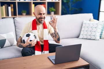 Hispanic man with tattoos watching football match hooligan holding ball on the laptop doing ok sign...