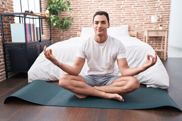 Fototapeta premium Young hispanic man doing yoga exercise sitting on floor at bedroom