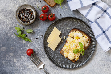 Scrambled eggs on whole grain bread on a stone table. Homemade breakfast or brunch meal - scrambled eggs. View from above.