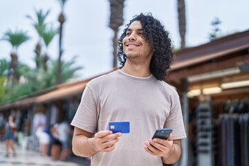 Young latin man using smartphone and credit card at street market
