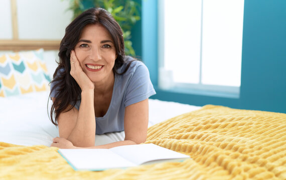 Middle age hispanic woman reading book lying on bed at bedroom
