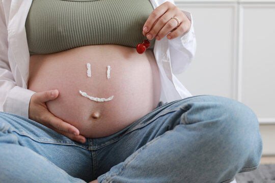 Close-up Of Torso Of Young Pregnant Model Applying Moisturizer On Her Belly To Avoid Stretch Marks. Future Mom With Funny Smile From Moisturizing Cream On Her Tummy. Pregnancy Skincare Concept