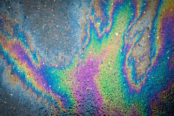 Close-up of an iridescent oil or gasoline spill on a wet asphalt, viewed from above. Bold multicolored spots on the asphalt. Concept of environmental problems