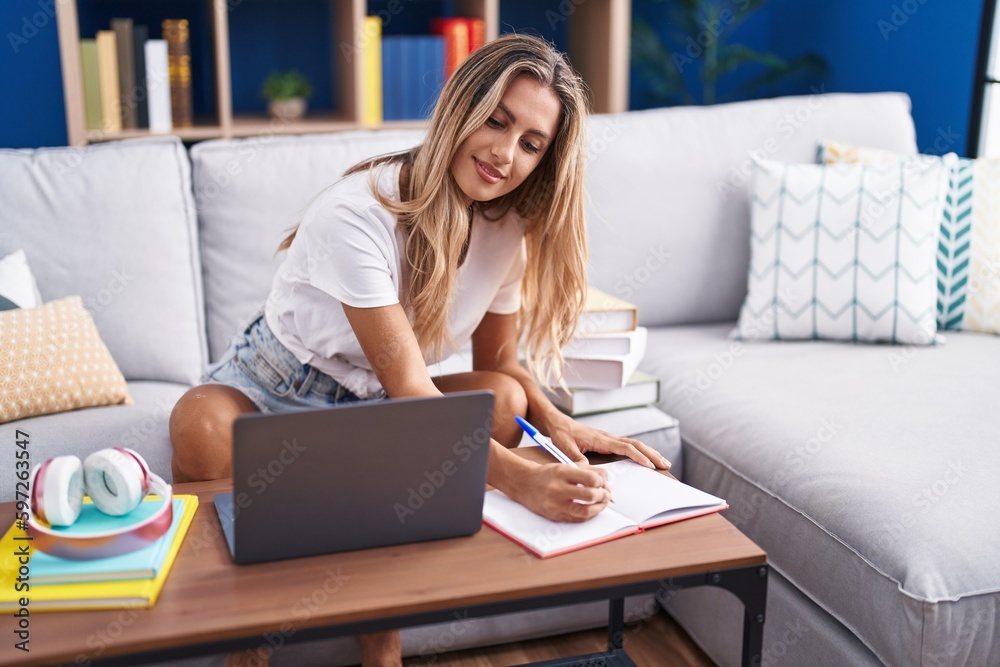 Canvas Prints Young blonde woman student sitting on sofa writing on notebook at home