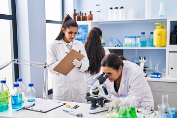 Obraz premium Three woman scientists using microscope write on checklist at laboratory