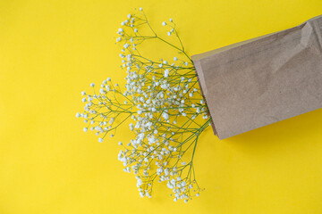 A bouquet of small gypsophila flowers in an eco bag on a yellow table Background with space for text
