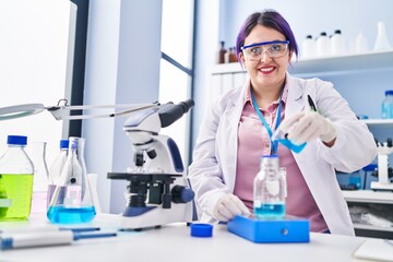 Young beautiful plus size woman scientist pouring liquid on test tube weighing liquid at laboratory