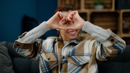 Obraz premium Middle age hispanic woman doing heart symbol with hands sitting on sofa at home
