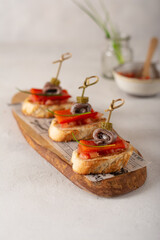 Plate of delicious Spanish tapas with marinated anchovies, backed paprika, tomatoes, pickles and herbs on slices of toasted bread.