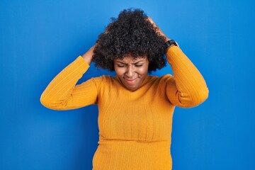Fototapeta na wymiar Black woman with curly hair standing over blue background suffering from headache desperate and stressed because pain and migraine. hands on head.