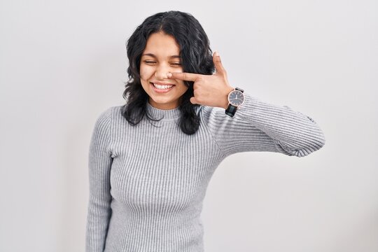 Hispanic woman with dark hair standing over isolated background pointing with hand finger to face and nose, smiling cheerful. beauty concept
