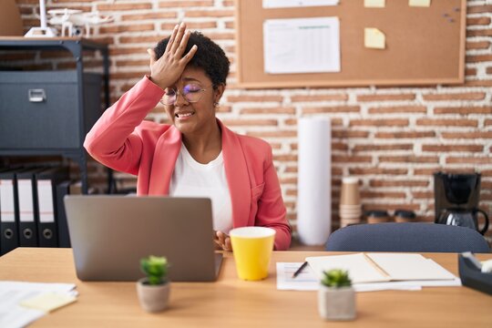 Young african american woman working at the office wearing glasses surprised with hand on head for mistake, remember error. forgot, bad memory concept.