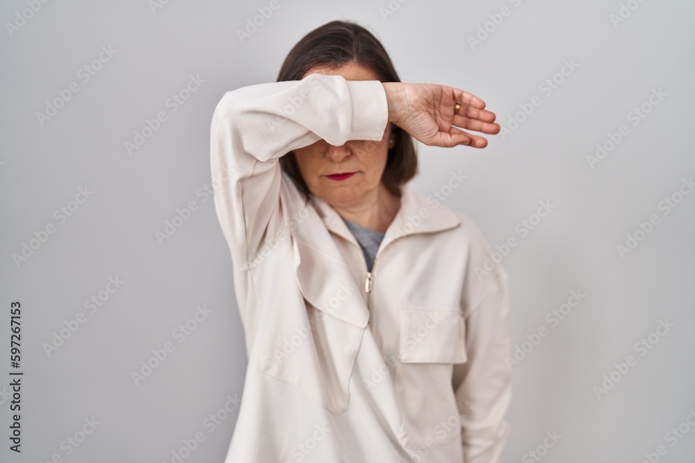 Wall mural middle age hispanic woman standing over isolated background covering eyes with arm, looking serious 