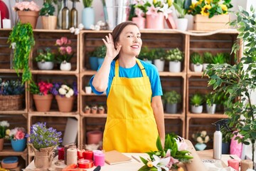Middle age hispanic woman working at florist shop smiling with hand over ear listening and hearing...