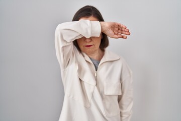 Middle age hispanic woman standing over isolated background covering eyes with arm, looking serious and sad. sightless, hiding and rejection concept